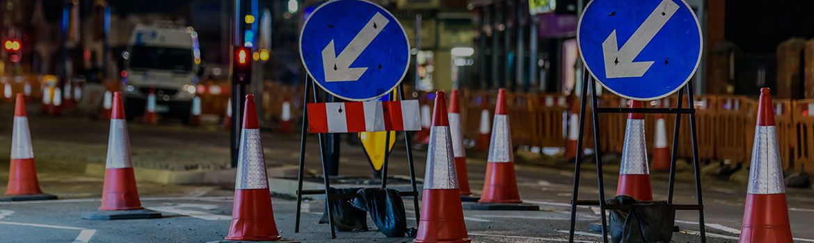 Services: Traffic cones signalling road work on a busy street at night.
